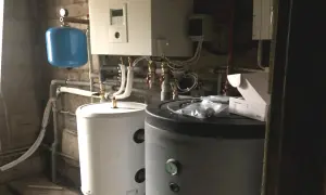 Podłączenie pompy ciepła do istniejącej instalacji. Widoczne zasobniki, sterownik i niebieski zbiornik wyrównawczy.
