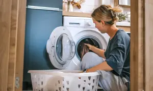 Kobieta wkłada pranie do pralki. Zastanawia się, ile kwh zużywa dom dziennie, gdy myśli o rachunkach.