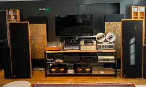 Zaawansowany system audio z dużymi kolumnami, gramofonem, magnetofonem szpulowym i wieloma wzmacniaczami. Dbałość o akustykę pomieszczenia widoczna w panelach rozpraszających.