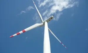 Białe wiatraki energetyczne z czerwonymi pasami na łopatach obracają się na tle błękitnego nieba z chmurami.
