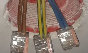 Trzy przewody w kostkach połączeniowych. Brązowe kable to plus i minus, żółto-zielony to uziemienie, a niebieski to przewód neutralny.