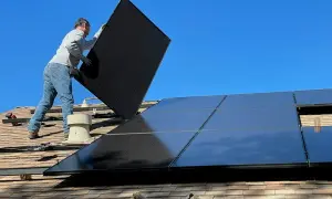 Pracownik montuje panele fotowoltaiczne na dachu, rozbudowa instalacji trwa.