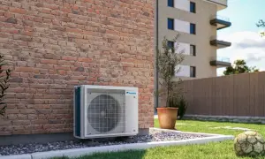 Jednostka zewnętrzna klimatyzatora Daikin przy ceglanej ścianie. Obok trawnik, donica z drzewkiem i stara piłka. Optymalizacja miesięcznego zużycia prądu w mieszkaniu.