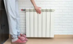 Osoba w kapciach dotyka kaloryfera, szukając sposobów, jak zaoszczędzić na ogrzewaniu.