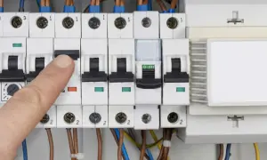 Palec naciska wyłącznik w skrzynce elektrycznej, co może oznaczać przebicie lub kontrolę zużycia prądu.