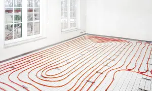 Instalacja ogrzewania podłogowego i grzejników na jednym obiegu. Pomarańczowe rurki ułożone na podłodze w pomieszczeniu z oknami.