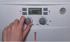 Dłoń reguluje pokrętłem temperaturę ciepłej wody użytkowej (CWU) na piecu. Wyświetlacz pokazuje 38.0°C.