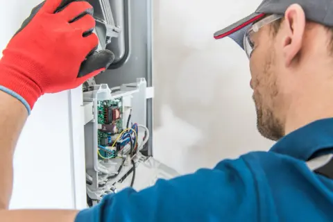 Technik w czerwonych rękawicach sprawdza wnętrze kotła, który wydaje dziwne odgłosy.