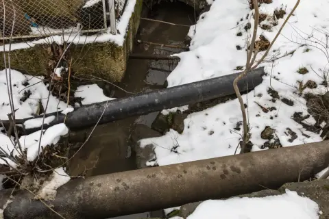 Zamarzanie rur w domku letniskowym. Dwa grube rury biegną nad strumieniem, a wokół leży śnieg.