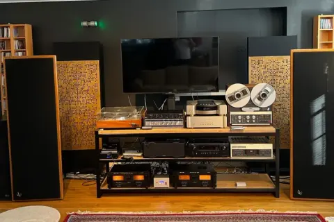 Zaawansowany system audio z dużymi kolumnami, gramofonem, magnetofonem szpulowym i wieloma wzmacniaczami. Dbałość o akustykę pomieszczenia widoczna w panelach rozpraszających.