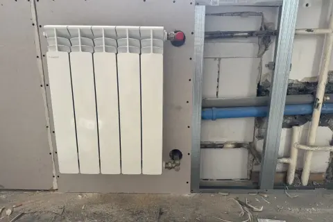 Nowy, biały grzejnik aluminiowy Fondital zamontowany na ścianie z płyty gipsowo-kartonowej. Trwa wymiana grzejnika żeliwnego na aluminiowy.