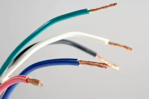 Różne kolory przewodów elektrycznych: zielony, biały, czarny, niebieski i różowy, z odsłoniętymi miedzianymi żyłami.