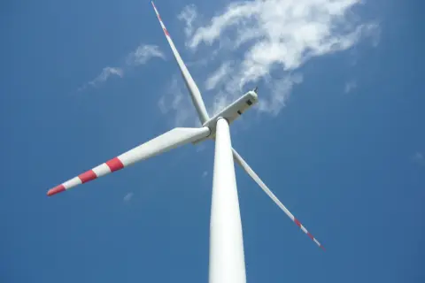 Białe wiatraki energetyczne z czerwonymi pasami na łopatach obracają się na tle błękitnego nieba z chmurami.
