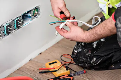 Elektryk przygotowuje przewody do podłączenia gniazdek. To faza prac remontowych.