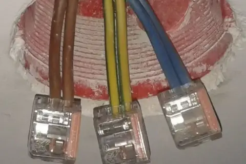 Trzy przewody elektryczne (brązowy, żółto-zielony, niebieski) połączone w puszkach. Czy faza to plus czy minus?