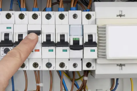 Palec naciska wyłącznik w skrzynce elektrycznej, co może oznaczać przebicie lub kontrolę zużycia prądu.