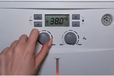 Dłoń reguluje pokrętłem temperaturę ciepłej wody użytkowej (CWU) na piecu. Wyświetlacz pokazuje 38.0°C.