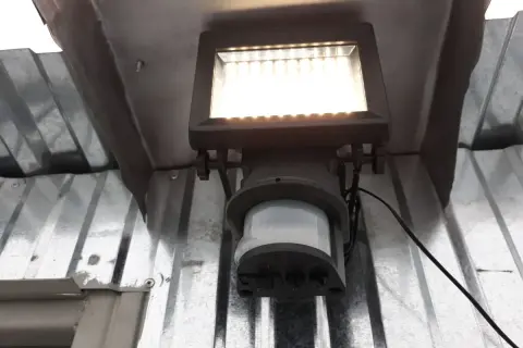 Lampa z czujnikiem ruchu sama się zapala, bo wykrywa ruch. Jasne światło oświetla metalową konstrukcję.