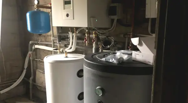 Podłączenie pompy ciepła do istniejącej instalacji. Widoczne zasobniki, sterownik i niebieski zbiornik wyrównawczy.