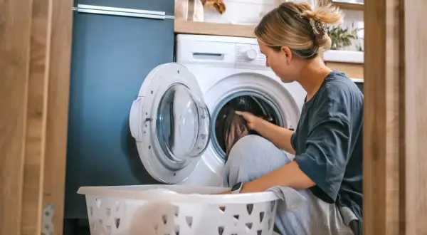 Kobieta wkłada pranie do pralki. Zastanawia się, ile kwh zużywa dom dziennie, gdy myśli o rachunkach.
