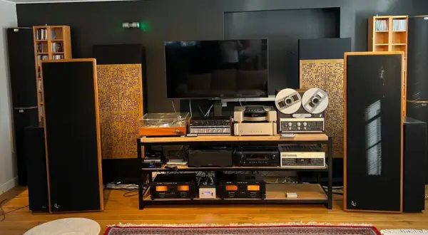 Zaawansowany system audio z dużymi kolumnami, gramofonem, magnetofonem szpulowym i wieloma wzmacniaczami. Dbałość o akustykę pomieszczenia widoczna w panelach rozpraszających.