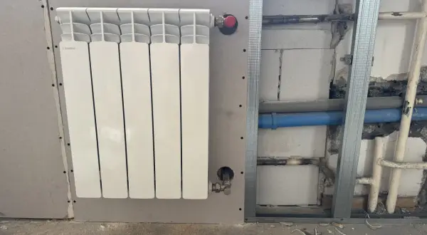Nowy, biały grzejnik aluminiowy Fondital zamontowany na ścianie z płyty gipsowo-kartonowej. Trwa wymiana grzejnika żeliwnego na aluminiowy.