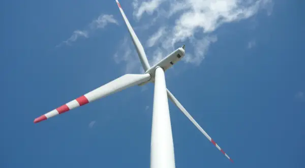 Białe wiatraki energetyczne z czerwonymi pasami na łopatach obracają się na tle błękitnego nieba z chmurami.