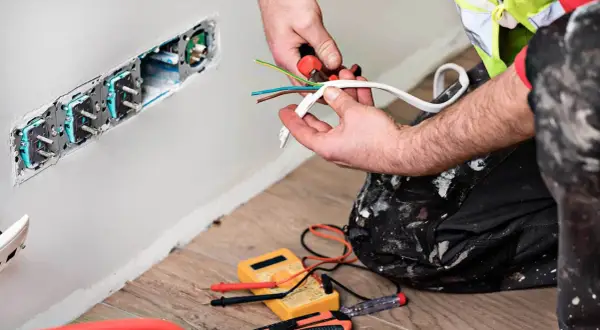 Elektryk przygotowuje przewody do podłączenia gniazdek. To faza prac remontowych.