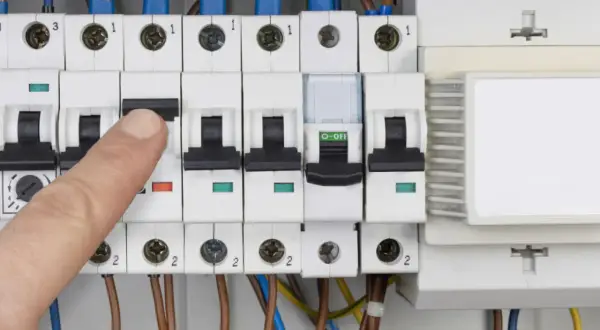 Palec naciska wyłącznik w skrzynce elektrycznej, co może oznaczać przebicie lub kontrolę zużycia prądu.