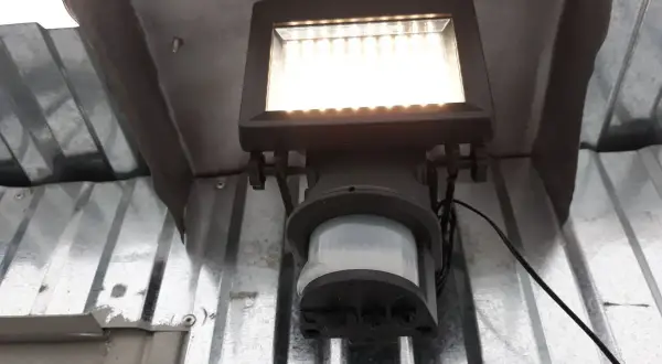 Lampa z czujnikiem ruchu sama się zapala, bo wykrywa ruch. Jasne światło oświetla metalową konstrukcję.