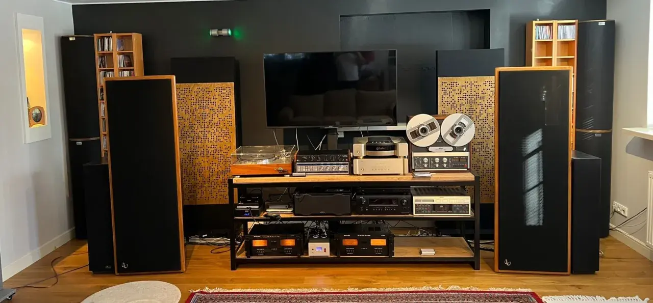 Zaawansowany system audio z dużymi kolumnami, gramofonem, magnetofonem szpulowym i wieloma wzmacniaczami. Dbałość o akustykę pomieszczenia widoczna w panelach rozpraszających.