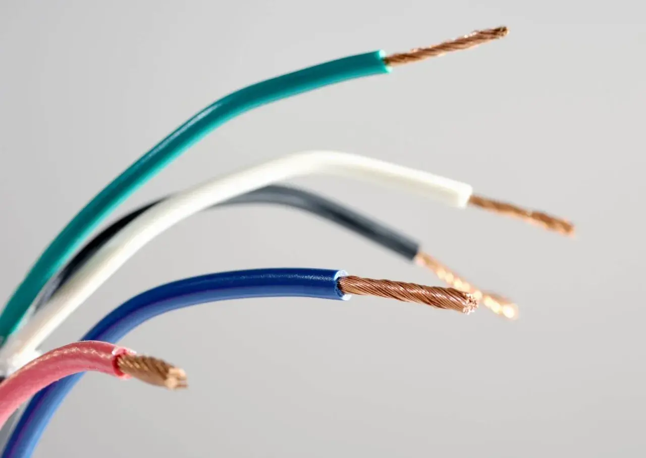 Różne kolory przewodów elektrycznych: zielony, biały, czarny, niebieski i różowy, z odsłoniętymi miedzianymi żyłami.
