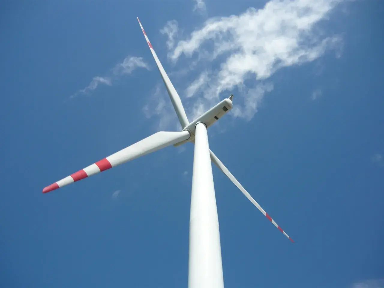 Białe wiatraki energetyczne z czerwonymi pasami na łopatach obracają się na tle błękitnego nieba z chmurami.