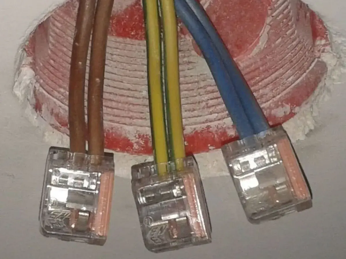 Trzy przewody w kostkach połączeniowych. Brązowe kable to plus i minus, żółto-zielony to uziemienie, a niebieski to przewód neutralny.