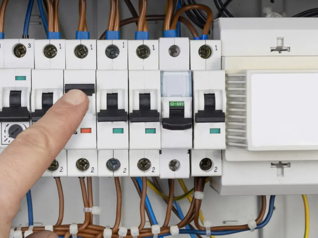 Palec naciska wyłącznik w skrzynce elektrycznej, co może oznaczać przebicie lub kontrolę zużycia prądu.