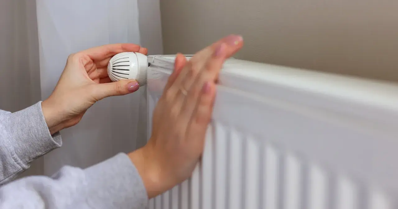Dłonie regulują termostat grzejnika. Kiedy wyłączyć ogrzewanie w domu, by oszczędzać energię?