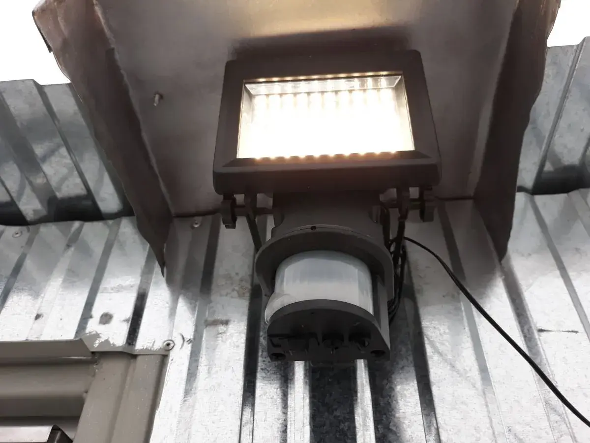 Lampa z czujnikiem ruchu sama się zapala, bo wykrywa ruch. Jasne światło oświetla metalową konstrukcję.