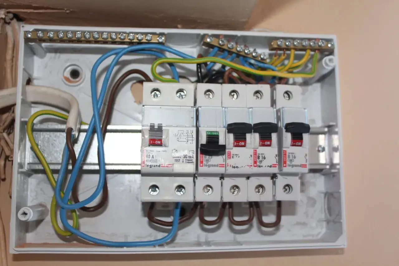 Rozdzielnica elektryczna z bezpiecznikami i przewodami. Widoczne przebicie izolacji na jednym z przewod&oacute;w, co może wpływać na zużycie prądu.