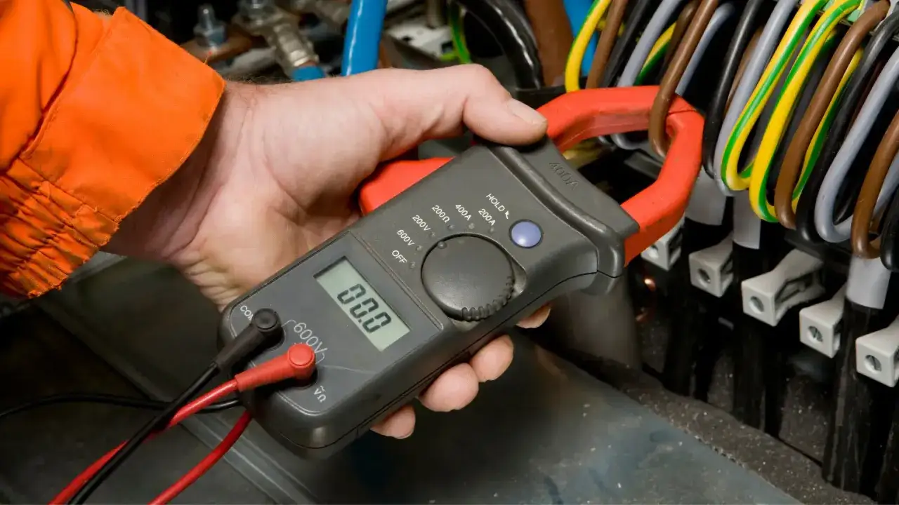Elektryk sprawdza, jakie powinno być napięcie w sieci, używając miernika cęgowego.