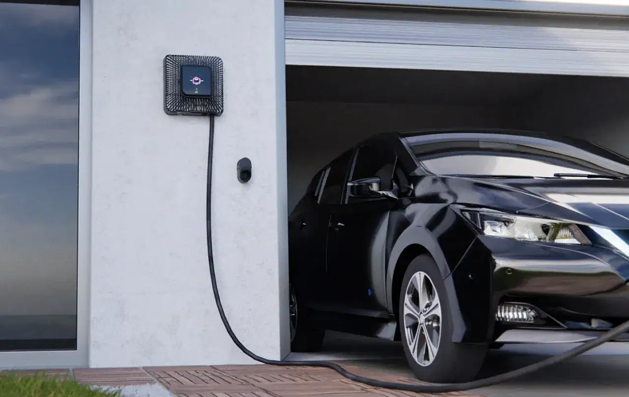 Czarny samoch&oacute;d elektryczny podłączony do ładowarki ściennej przy garażu.