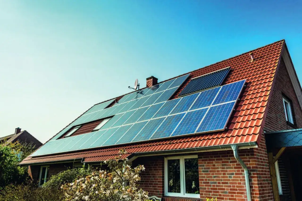 Dom z panelami fotowoltaicznymi i kolektorem słonecznym na dachu. To rozwiązanie pokazuje, co to jest kolektor słoneczny i jak można wykorzystać energię odnawialną.