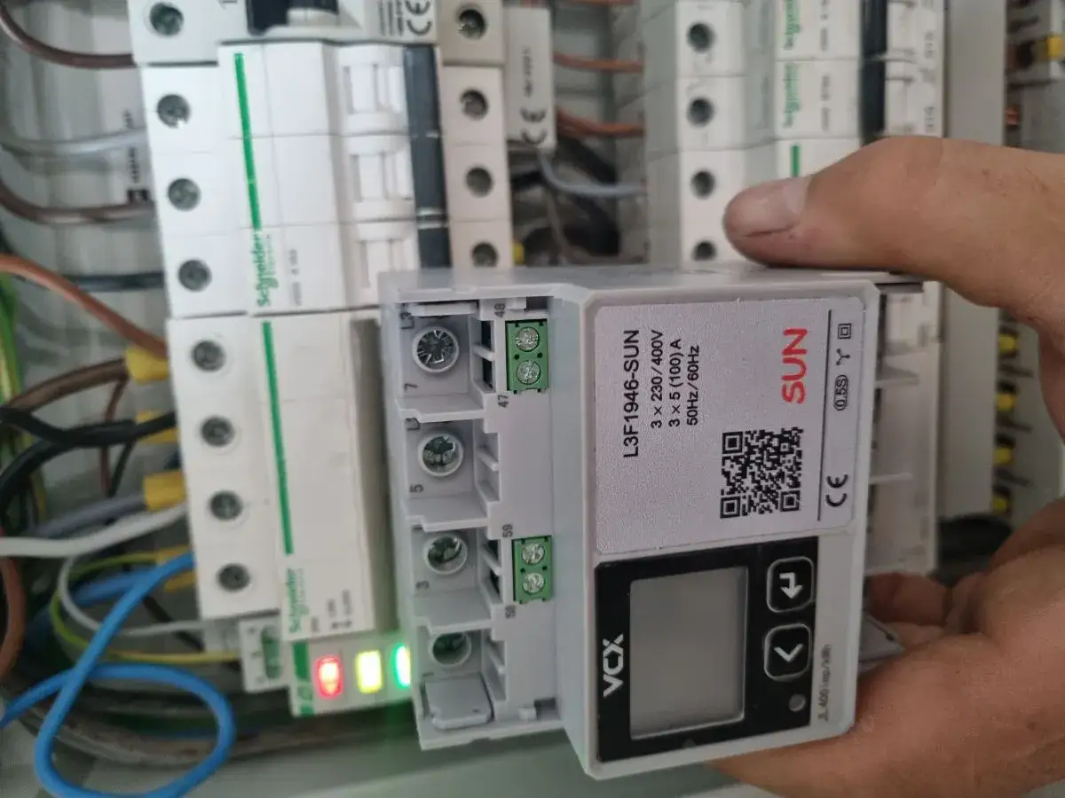 Instalacja podlicznika prądu. Ręka trzyma moduł licznika SUN L3F1946-SUN obok wyłączników Schneider.