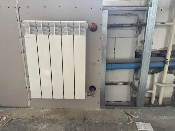 Nowy, biały grzejnik aluminiowy Fondital zamontowany na ścianie z płyty gipsowo-kartonowej. Trwa wymiana grzejnika żeliwnego na aluminiowy.
