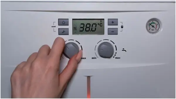 Dłoń reguluje pokrętłem temperaturę ciepłej wody użytkowej (CWU) na piecu. Wyświetlacz pokazuje 38.0°C.